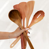 Hand holding a set of wooden cooking utensils against a white background