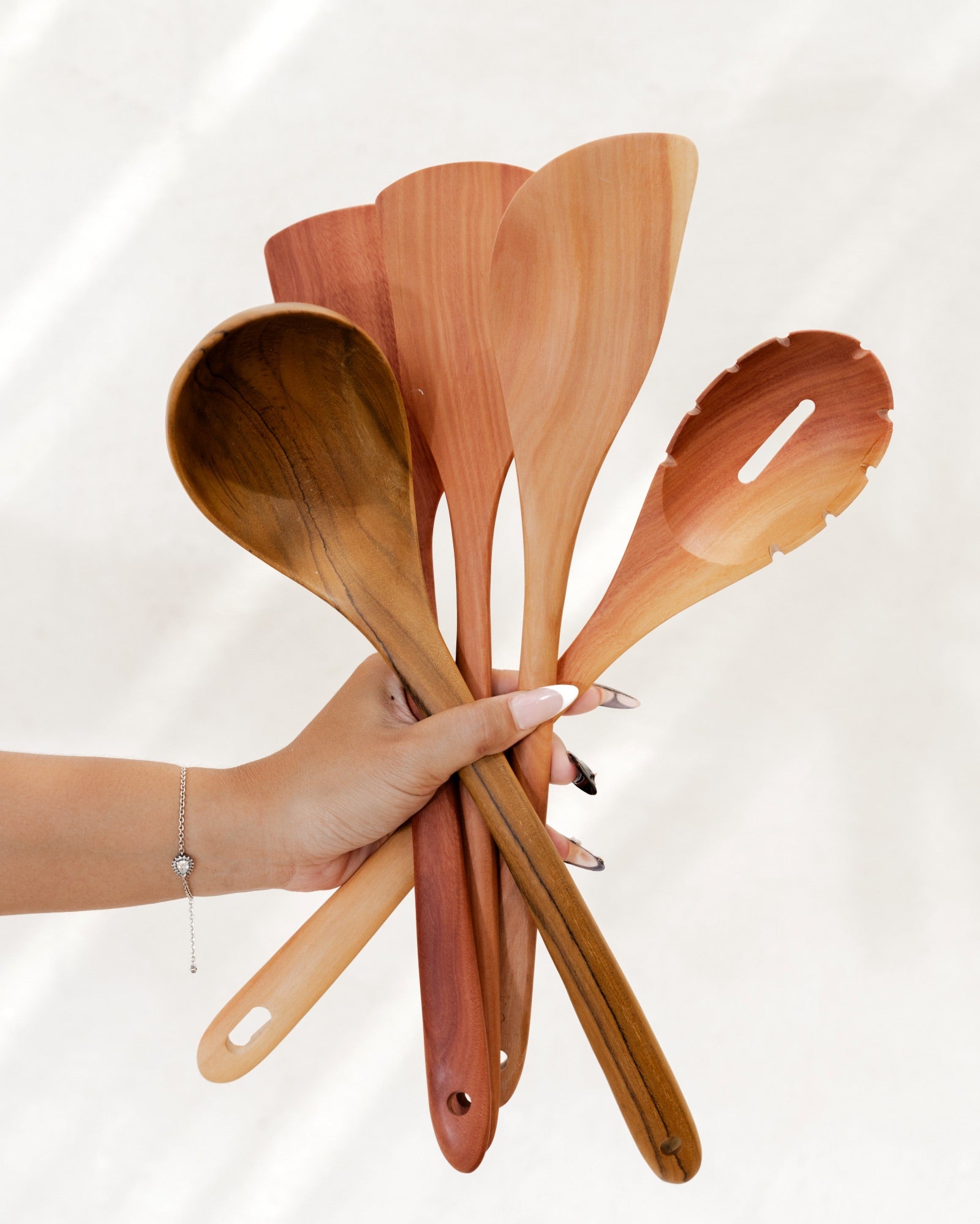 Hand holding a set of wooden cooking utensils against a white background