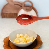White bowl with pineapple chunks on a wooden tray, wooden spoon above