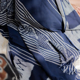 A close-up of a navy blue and white patterned fabric, likely a scarf or shawl, featuring stripes, ikat motifs, and fringed edges.