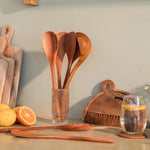 Wooden kitchen utensils in a glass holder on a kitchen counter with a glass of coffee and oranges.