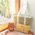 Woven bags including a large tote, small crossbody, and clutch on a textured surface with a blurred natural background.