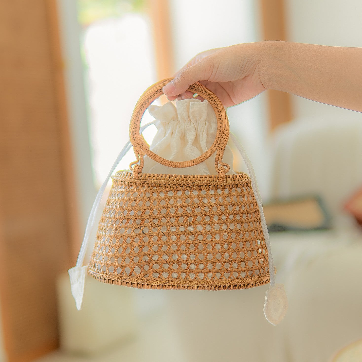 Hand holding Camilla circle bag with a blurred indoor background