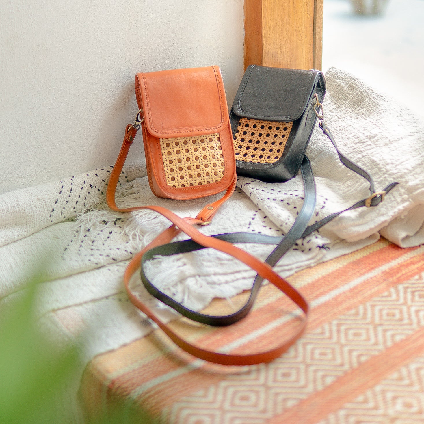 Two handbags, one orange and one black with wicker accents, on a textured surface.