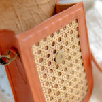 Close-up of a brown handbag with sued inner fabric and a textured pattern. Warm tan Harper phone bag on woven textile