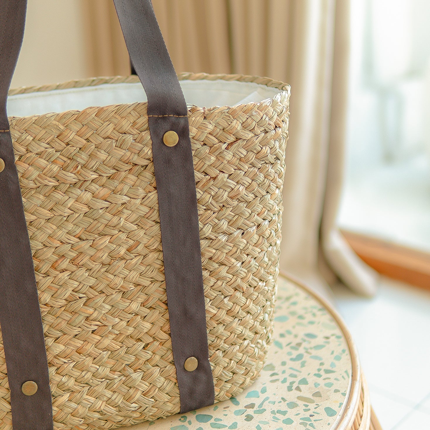 Woven straw bag with brown cotton straps on a surface