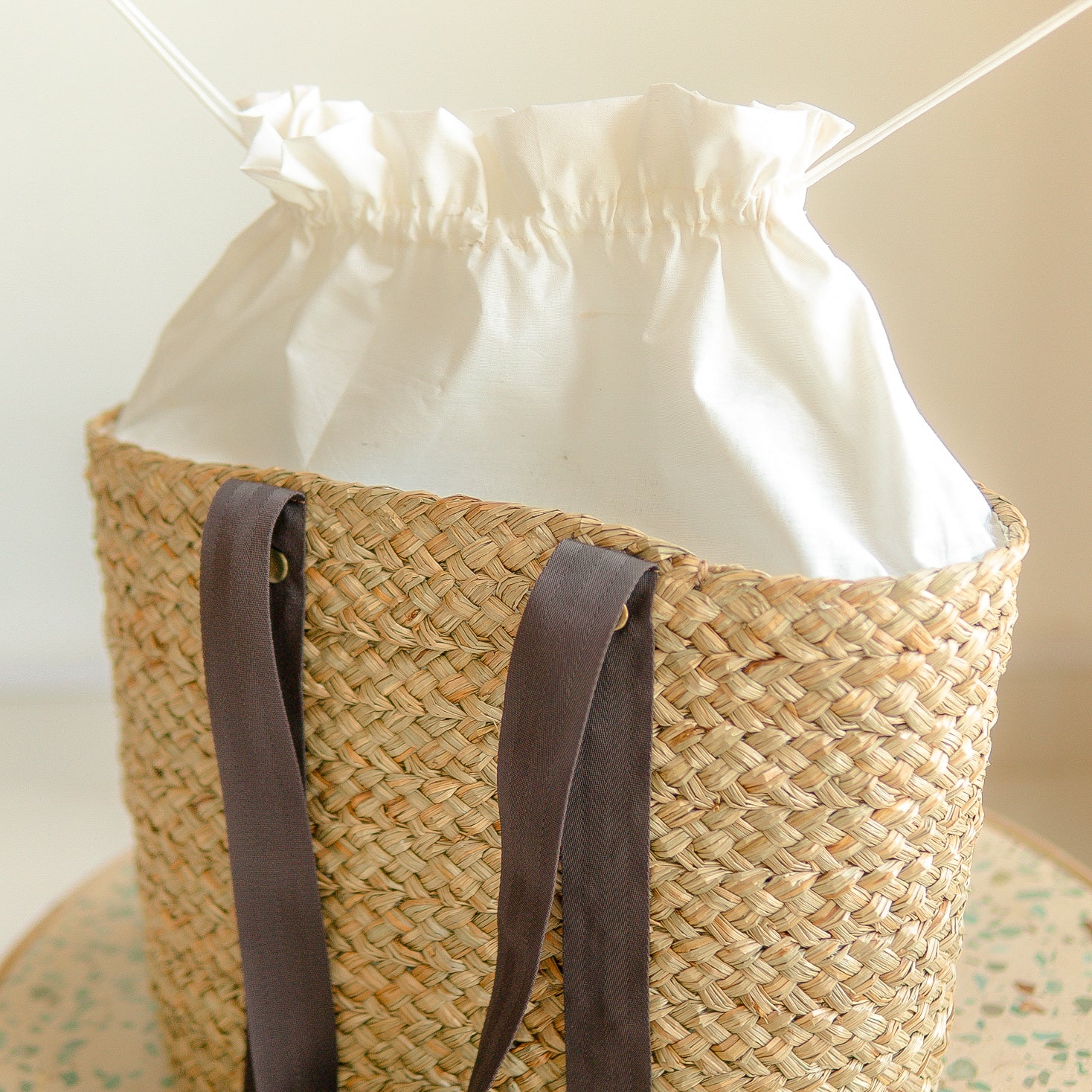 Woven basket with a white drawstring bag inside, on a neutral background
