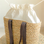Woven basket with a white drawstring bag inside, on a neutral background