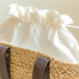 White blouse with ruffled sleeves and a straw bag with a brown cotton strap on a light background