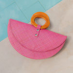 Pink straw bag with orange handle on a light blue and beige background