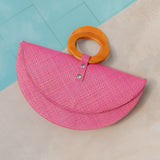 Pink straw bag with orange handle on a light blue and beige background