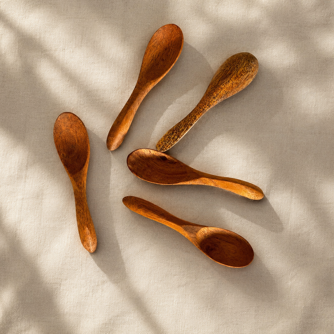 Five wooden spoons in varying sizes arranged on a textured cream fabric with soft leaf shadows cast across them.