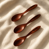 Three dark brown wooden spoons arranged diagonally on a textured cream fabric background with soft shadows.