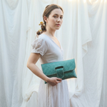 Woman holding a teal clutch against a white curtain background