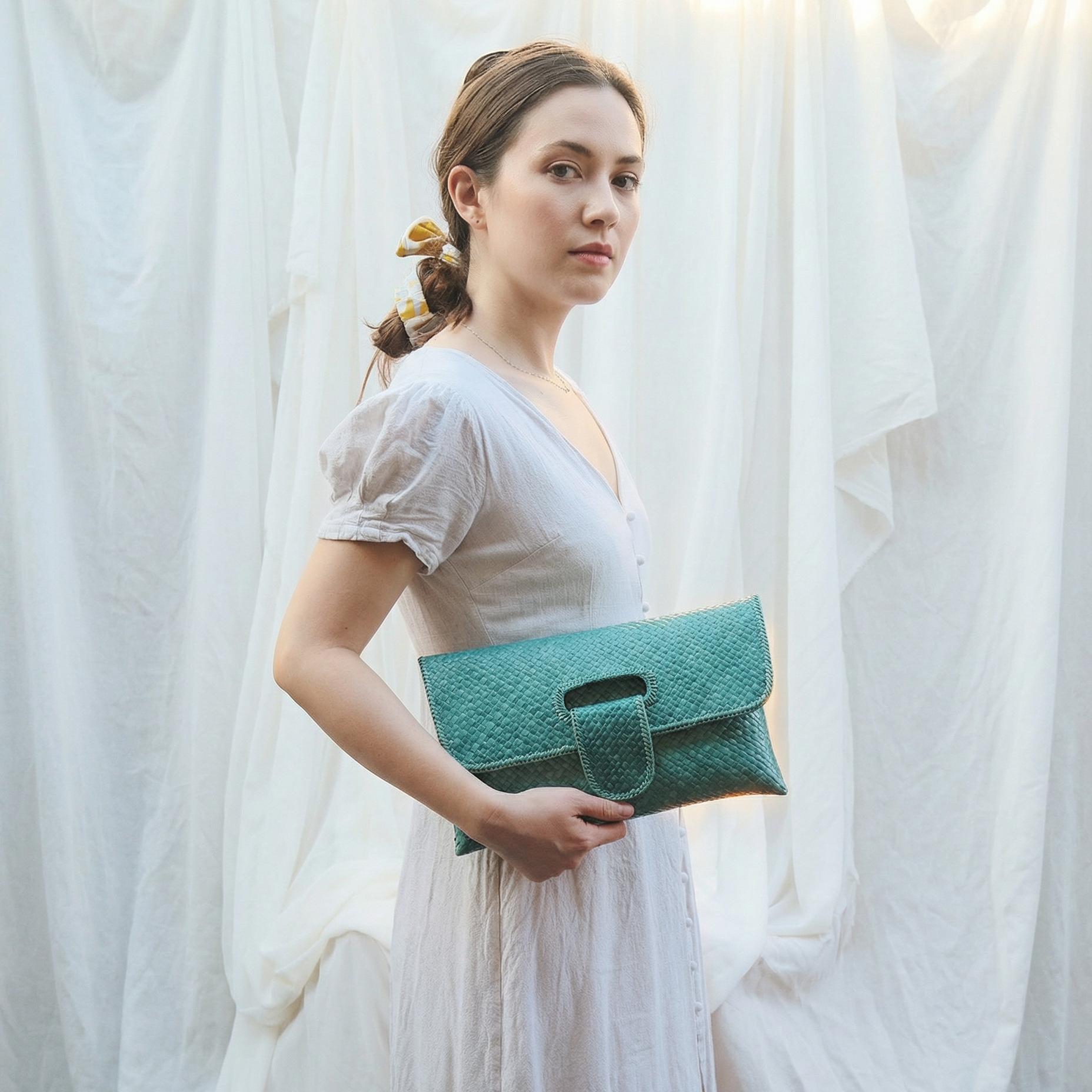 Woman holding a teal clutch against a white curtain background