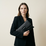 Woman holding a black clutch with a textured pattern against a beige background
