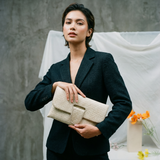 Woman holding a beige clutch against a neutral background