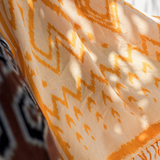 Close-up of a patterned orange and beige fabric with fringes.