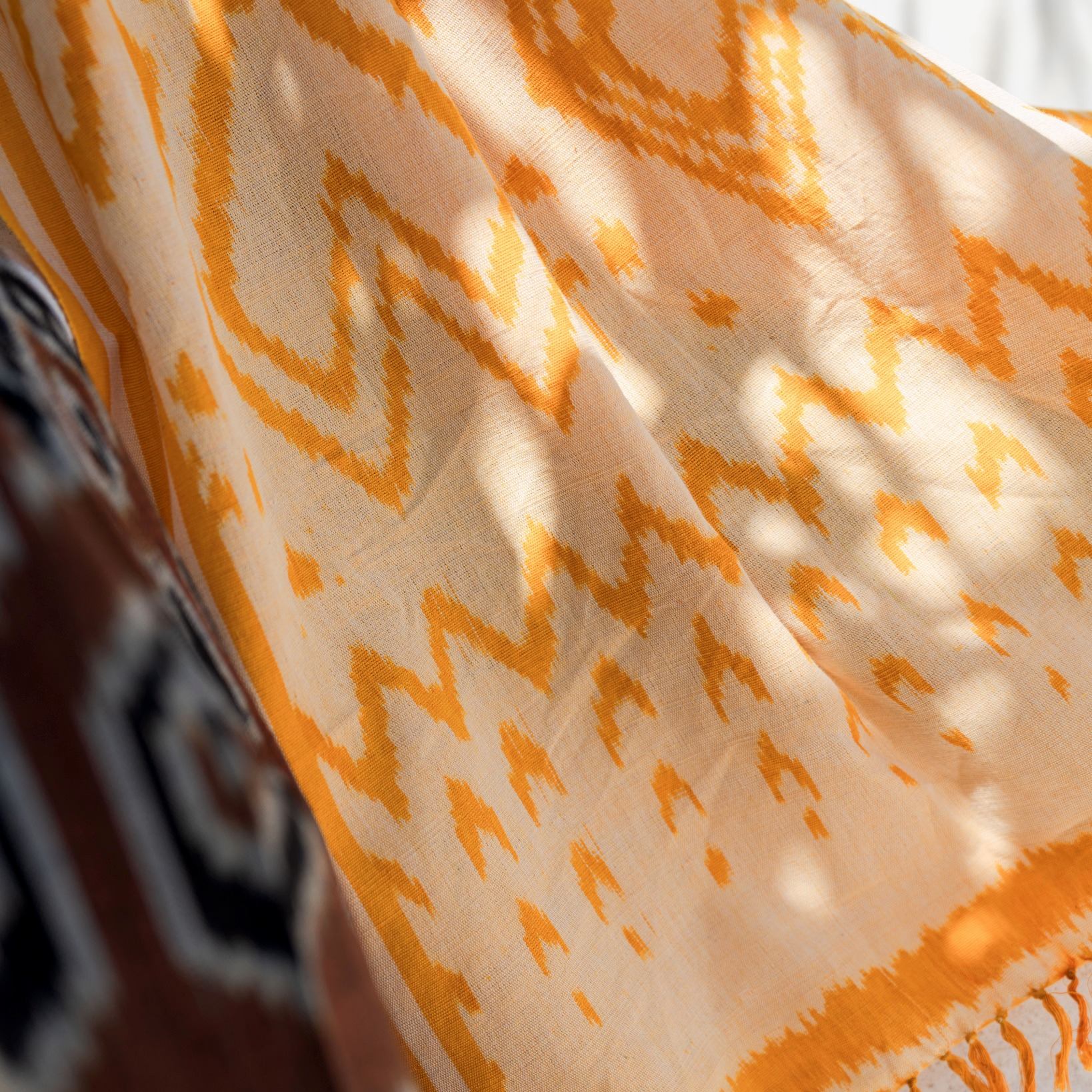 Close-up of a patterned orange and beige fabric with fringes.