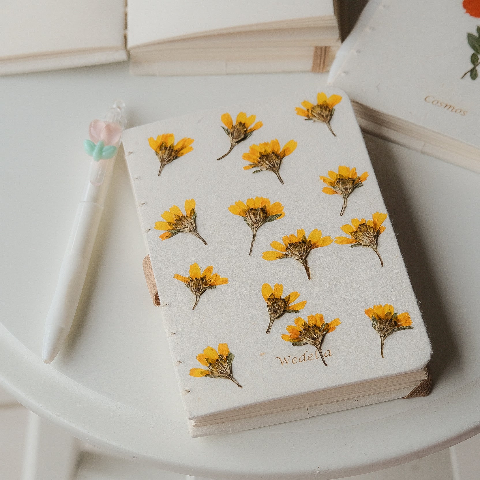 A6 journal with real dried Wedelia flowers on the cover, white floral pen, and soft fabric pouch – sustainable stationery gift